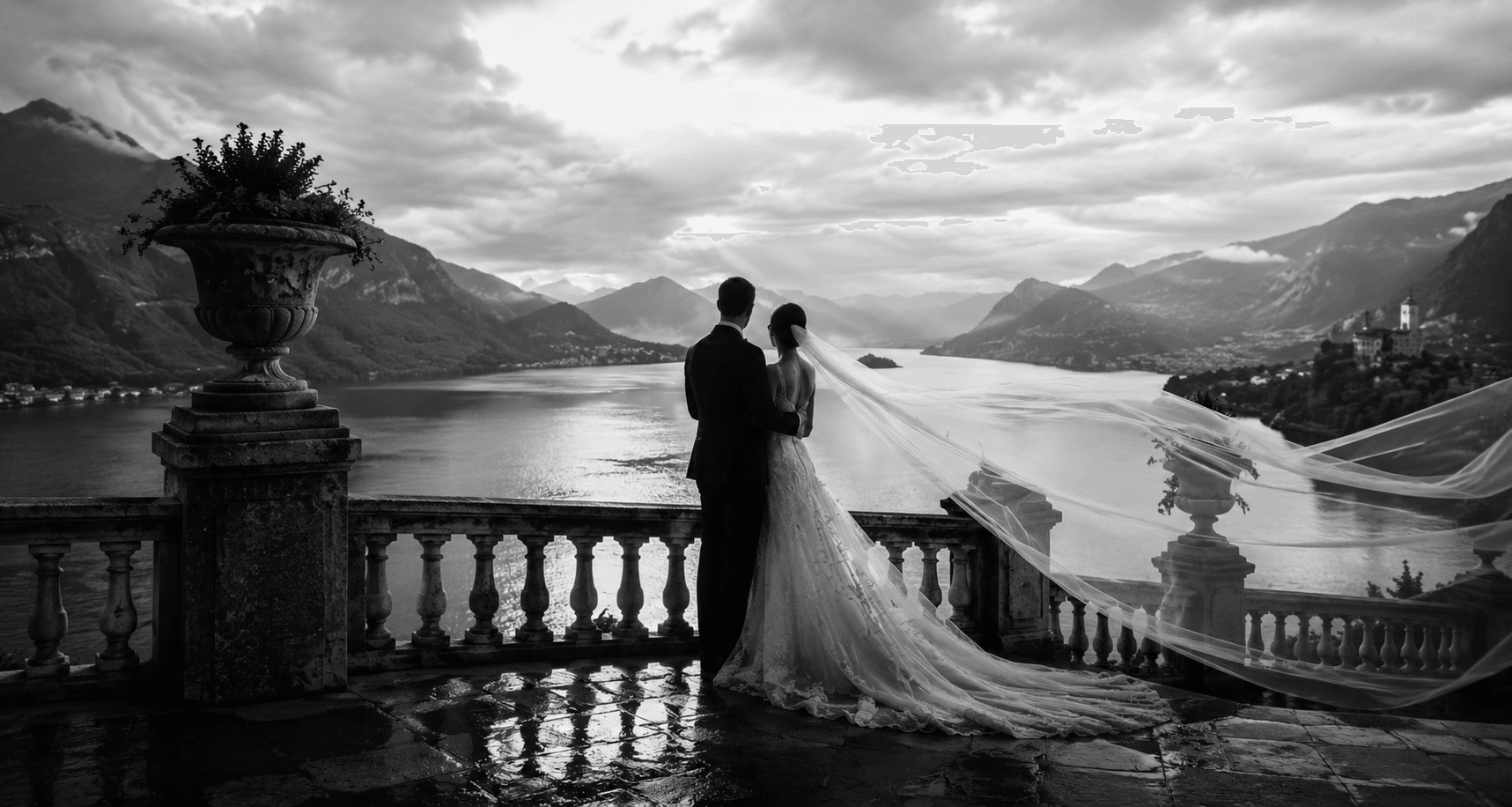 Brautpaar in Schwarz-Weiss auf einer Terrasse mit Blick auf einen Bergsee, der Schleier weht im Wind